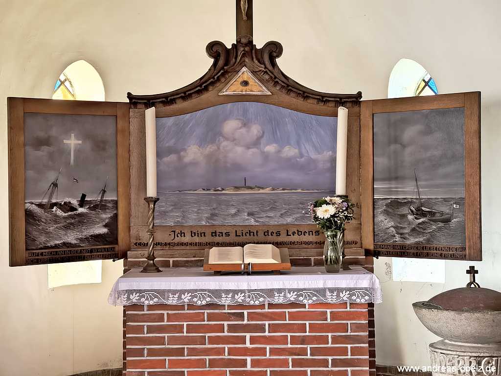 Amrum Insel-Orte und Dörfer:Kapelle in Wittdün, der dreigliedrige Altaraufsatz mit dem Bild von der Südspitze mit dem Amrumer Leuchtturm, einem Bild mit einem Rettungsboot im Einsatz auf der rechten Seite und mit dem Bils eines gestrandeten Schiffes auf der linken Seite Die Kapelle in Wittdün auf Amrum: der dreigliedrige Altaraufsatz mit dem Bild von der Südspitze mit dem Amrumer Leuchtturm, einem Bild mit einem Rettungsboot im Einsatz auf der rechten Seite und mit dem Bils eines gestrandeten Schiffes auf der linken Seite